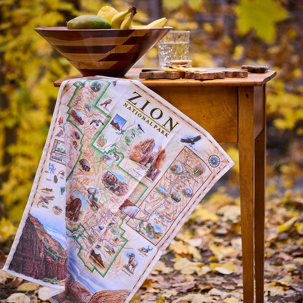 Zion National Park map on a wooden table with a bowl of fruit and snacks in an outdoor setting.