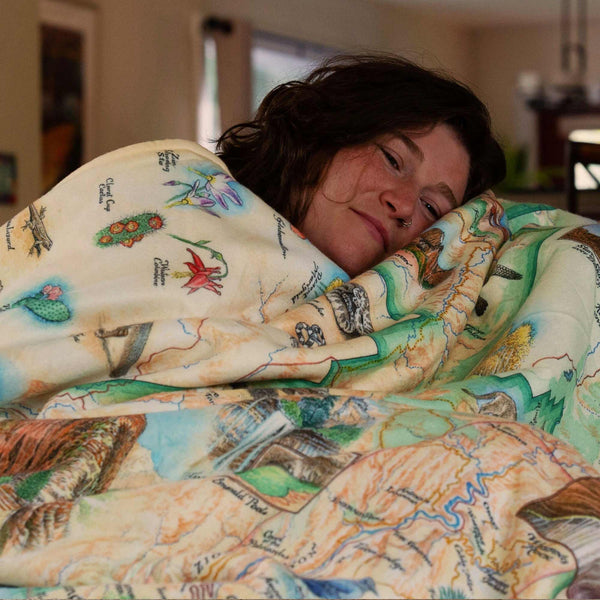 Person wrapped in a colorful quilt with nature-themed patterns in a home setting.