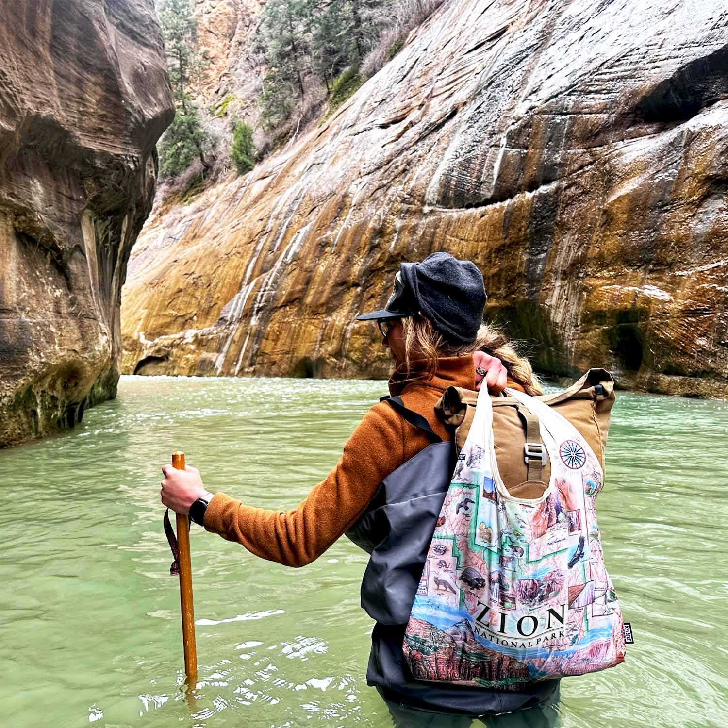 Women walking in a river canyon in Zion with the Zion National Park pouch tote back over her shoulder. 