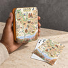 A hand holds a small illustrated metal tin labeled Zion National Park, with matching playing cards placed on a stone surface in front. The product appears to be a Zion National Park themed card deck or set, shown in a real tabletop setting.