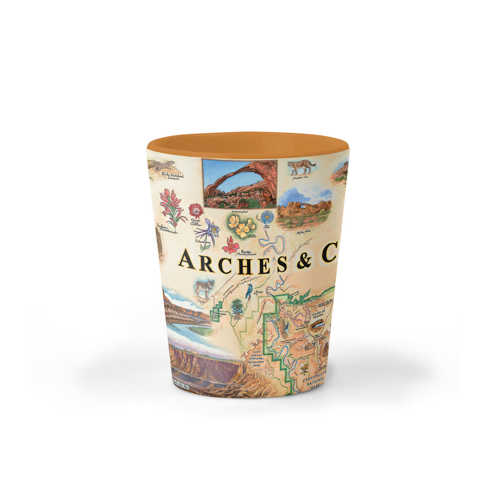 Utah's Arches & Canyonlands National Parks map ceramic shot glass in earth tone colors. Arches & Canyonlands National Parks map ceramic shot glass in earth tone colors of blues and greens. The map features deer, mountain lion, porcupine, bobcats, and a fox. Landmarks are Tower Arch Delicate Arch, Double O Arch, Balanced Rock, Island in the Sky, and Fiery Furnace. 