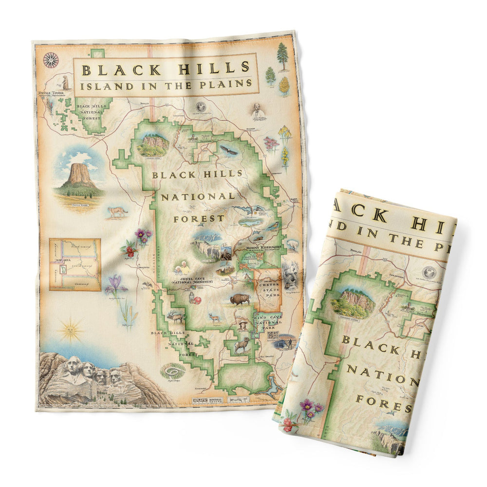Black Hills National Forest Map Kitchen Towel in earth tone colors. It features cities like Rapid City, Spearhead, Rapid City, and Sturgis. Mount Rushmore, Devils Tower, Jewel Cave National Monument, Custards, and Wind Cave National Park. Flora and Fauna illustrations include bison, elk, mountain goats, birds, pine trees, and native flowers. 