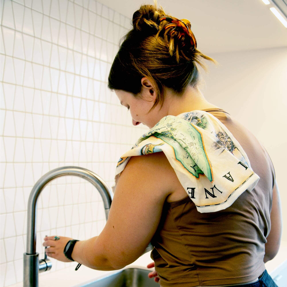 Maine State Map kitchen dishtowel hanging over a women's shoulder while washing dishes. 