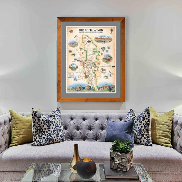 Red Rock Canyon National Recreation Area hand-drawn map in a Montana Flathead Lake Larch frame and gray-purple mat. The print hangs over a purple couch with blue and lime green pillows. 